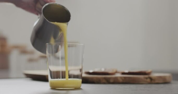 Slow motion man hand pour mango lulo smoothie into tumbler glass on concrete countertop with copy space