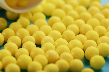 Yellow vitamin C capsules spilled out of a white jar against a blue background.
