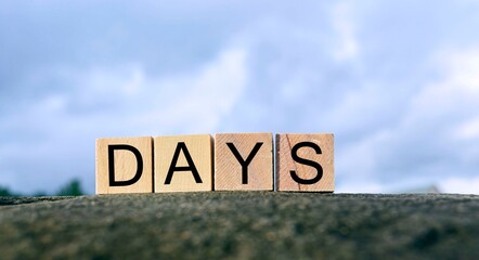 Obraz premium Days text on wooden block on top of big stone with blurred sky background