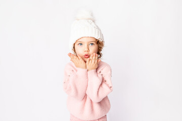 cute baby girl in pink winter clothes on a white background blows off her hands, space for text