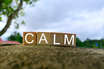Calm text on wooden block on top of big stone with blurred sky background