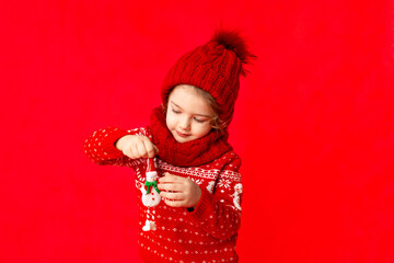a little girl in winter clothes holds a snowman on a red background. New year's concept, space for text