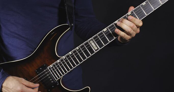 Unrecognizable rock musician with in dark-blue shirt plays brown electric guitar on black background isolated and smoke. 