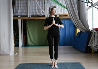 Serene young woman in sportswear standing on legs while practicing tree pose in cozy living room during quarantine