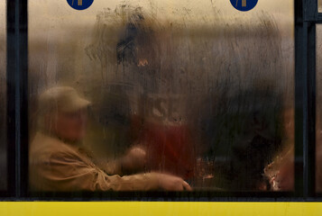 retired with a cane rides a city bus in rainy evening behind misted glass