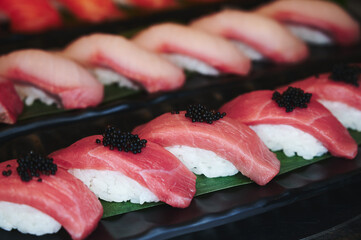 Tuna sushi with black tobiko on a black dish. Blurry hamachi sushi in the background.