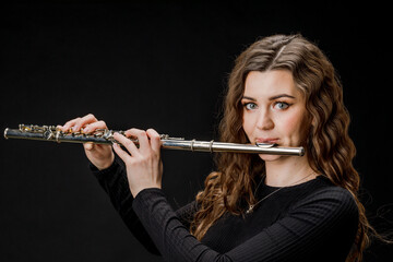Portrait of a woman playing a transverse flute, isolated on a black background.