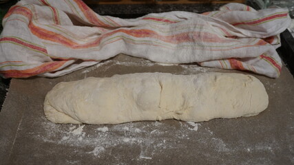 Teig, Teigrohling für ein Baguette, Ciabatta, Weißbrot in langer Form mit Mehl bestäubt, fertig zum Backen