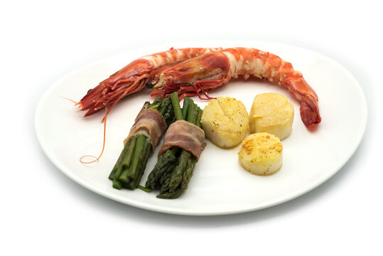 Closeup of shelled prawns, st jaques and asparagus in a plate on white background
