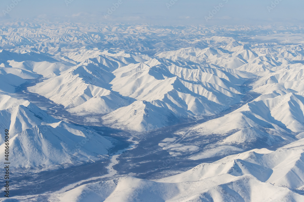 Wall mural Aerial view of snow-capped mountains. Winter snowy mountain landscape. Air travel to the far North of Russia. Kolyma Mountains, Magadan Region, Siberia, Russian Far East. Great for the background.