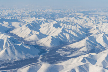 Aerial view of snow-capped mountains. Winter snowy mountain landscape. Air travel to the far North...