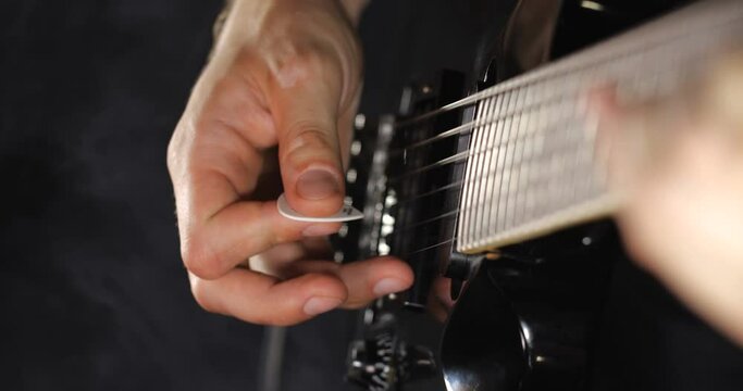Unrecognizable rock musician in black clothes plays black electric guitar on black background isolated and smoke. Close up of hand and soundboard
