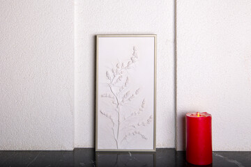 Botanical bas-relief wildflowers for wall art and red christmas candle on marble shelf. 3D Flower plaster decor. Christmas decoration. Stylish and modern interior of room.