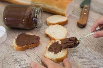 Hands spreading chocolate paste on a baguette.