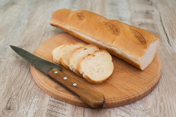 baguette with a knife and a cutting board on wooden table.
