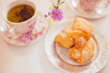 Crispy croissants on a silver vintage plate and tea cups on the white table
