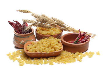 Pasta cornetti creste macaroni pile in clay pot, with dried peppers and ear of wheat isolated on...