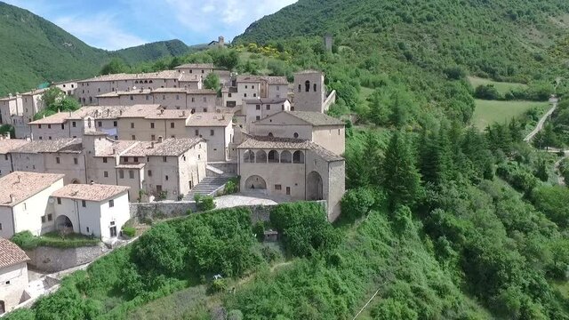 Aerial drone view of a small village or group of houses on a hill surrounded by green plants and trees.