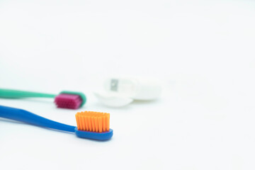 Two colored toothbrushes with bright orange and red bristles and dental floss lie on a white background, daily oral care