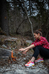 girl in red shirt and black jeans sitting in front of fire in forest. Human and nature. Traveler girl alone on mountain. Feeling freedom in camp.