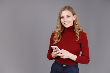 Portrait of cheerful young girl using mobile phone isolated over grey background