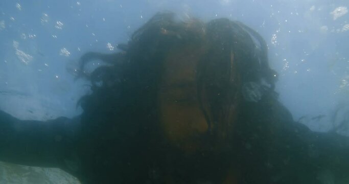 Close-up underwater shot of a  long-haired man  in black clothes lying in the water and drowned surrounded by jellyfish. The concept of lost hope and suicide. 4k slow motion