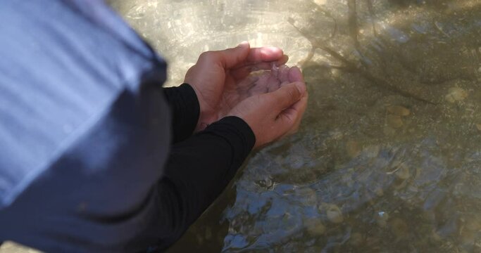 Close up detail thirsty wanderer greedily drinking life-giving water from a stream or lake. Hands of long-haired man in dirty dark clothes  collects clear water from the lake. 4K 50 fps slow motion.