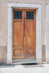 Italian retro wood style front door, the main entrance on the sandy yellow color wall facade. Element of the classic Italian facade and architecture