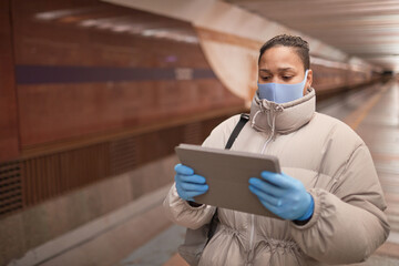 Fototapeta na wymiar Woman in protective mask and gloves using digital tablet while walking along in the underground