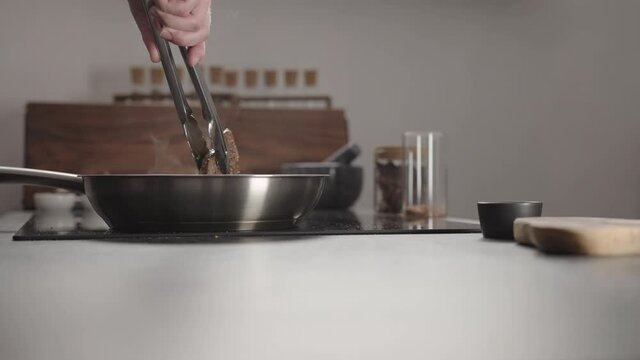 Man frying beef steak searing side on steel pan on electric hob on kitchen