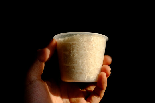 hand holding cup full of rice isolated on black background