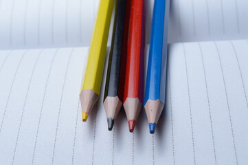 four multi-colored pencils - blue, red, yellow, black. lie on an open notebook.