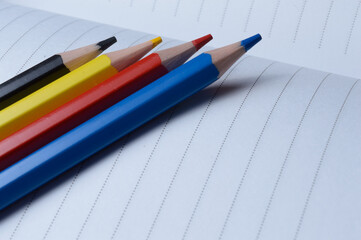 four multi-colored pencils - blue, red, yellow, black. lie on an open notebook.