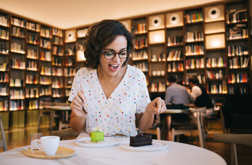 Exited woman enjoying desserts in cafe of book store