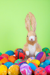 rabbit figurine between painted easter eggs before green background