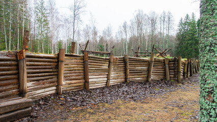 Wooden military fence in the forest. Fence with barbed wire.