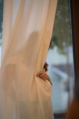 girl hides behind the window curtain, shyness concept