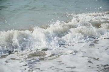 Ocean waves splashing onto the shore of a sandy beach causing white foam and bubbles