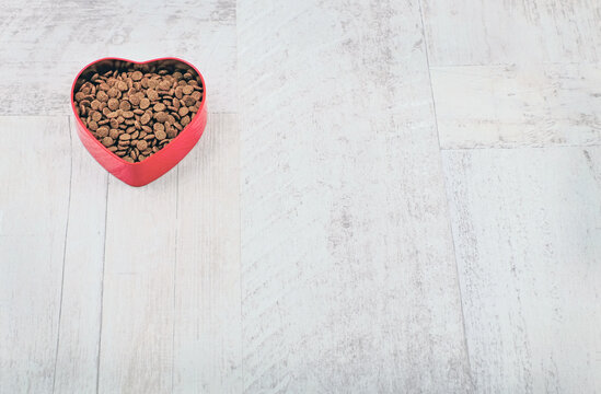 Heart shaped bowl with food for pets on wooden background. With care for animals concept and Valentine's Day. Copy space