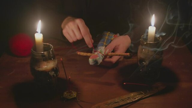 Close up of mysterious wizard male fortune teller uses voodoo doll and red rope to terrible magic ritual in dark