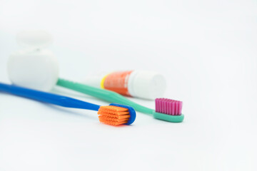Two bright multi colored toothbrushes, a tube of toothpaste and dental floss on a white background on the left side,  oral care in daily routine 