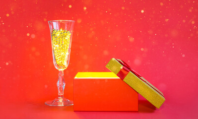 Open red gift box with golden glow and glitter inside and champagne glass with bubble beads, banner, copyspace. universal holiday, christmas, valentine's day, new year, birthday, anniversary, present