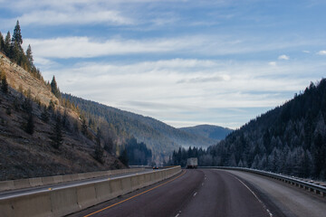 An asphalt road along which cars and trucks go, among the mountains, ahead on the horizon mountains in fog, the sky is covered with clouds. Idaho, USA, 11-23-2019