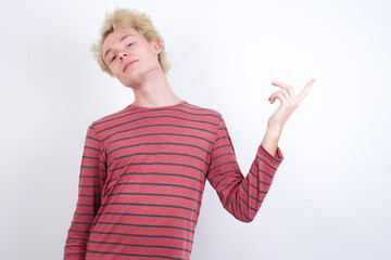 Smiling Young handsome Caucasian blond man standing against white background indicating finger empty space showing best low prices