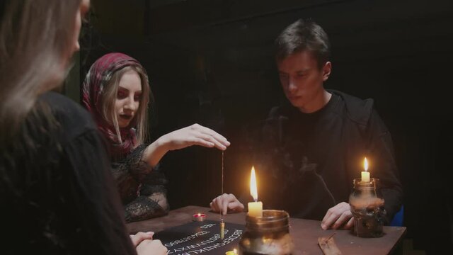 Witch female fortune teller tries to speak with ghost. Two women and one man uses Ouija Board Spirit Game
