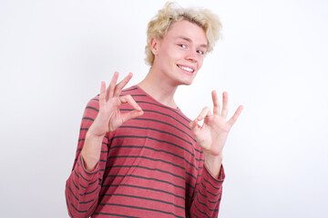 Young handsome Caucasian blond man standing against white background showing both hands with fingers in OK sign. Approval or recommending concept