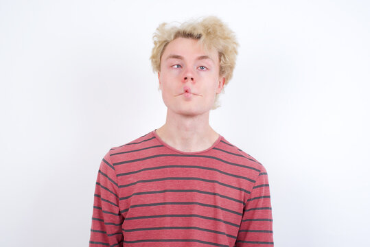 Young handsome Caucasian blond man standing against white background making fish face with lips, crazy and comical gesture. Funny expression.