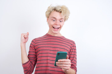 Portrait of Young handsome Caucasian blond man standing against white background holding in hands cell celebrating