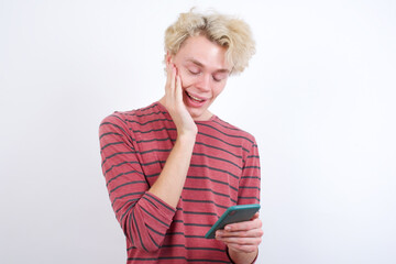 Young handsome Caucasian blond man standing against white background holding in hands cell reading sms using new app 5g