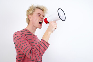 Young handsome Caucasian blond man standing against white background speaking  Through Megaphone with Available Copy Space